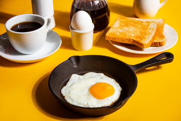 Fried egg on pan, black coffee, toasts on yellow background. Retro American breakfast. Hard shadow.