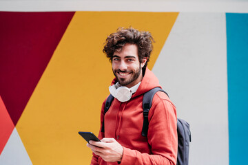 Smiling young man with smart phone in front of colorful wall