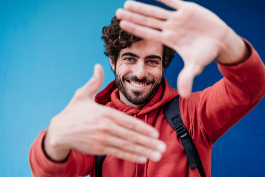Happy man making finger frame in front of blue wall