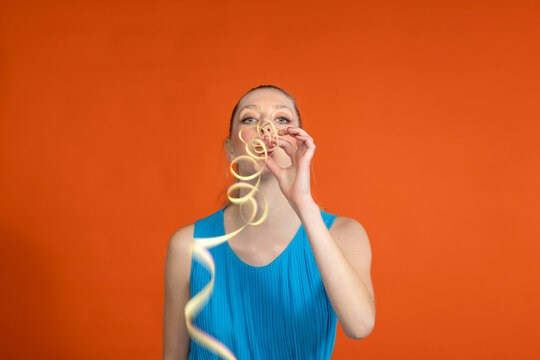 Playful young woman blowing streamer against orange background