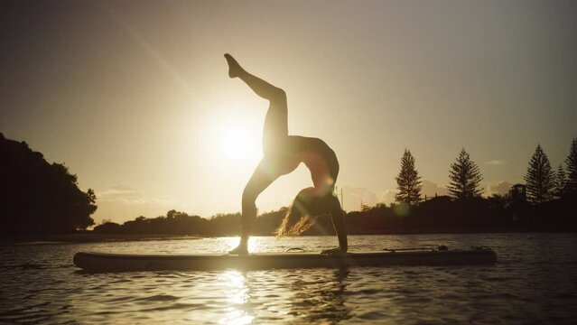 A Young Beautiful Fit woman Practicing Paddle Board yoga at sunset
