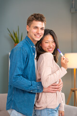 Happy multi-ethnic couple showing positive pregnancy test result looking at camera happy smiling. Future parents, woman and man expecting a baby waiting for a child. Motherhood love concept