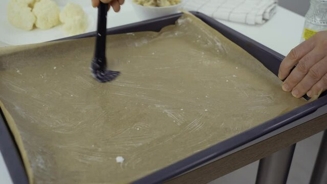 Grease a baking tray lined with baking paper with coconut oil using a brush. Close-up.