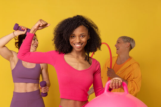 Smiling woman flexing muscles standing with friends against yellow background