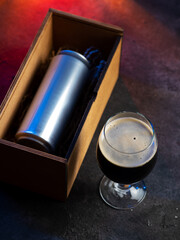Craft beer can in a wooden gift box. Dark beer glass on a black table