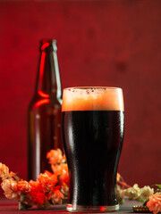 A dark craft beer glass . Red background. Beer bottle and hops
