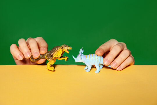 Man playing with dinosaur figurines on yellow table against green background