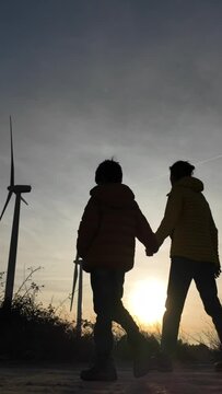 Mother with son walk through a renewable energy wind farm during the sunset. Silhouette of people and wind turbine. Concept sustainability, climate change, saving the earth. green energy and zero emis