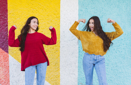 Smiling sisters flexing muscles in front of multi colored wall