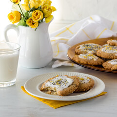 A plate of lemon poppyseed cookies with a bite out of one, served with milk.