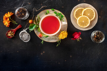 Tea with various ingredients and copy space. Herbs, fruits, and flowers, top shot on a black background. Healthy natural remedies