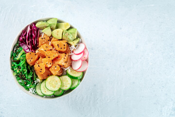 Salmon poke bowl with avocado, cucumbers, wakame, radish, and purple cabbage, top shot with copy...