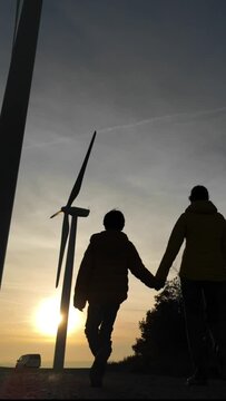 Mother with son walk through a renewable energy wind farm during the sunset. Silhouette of people and wind turbine. Concept sustainability, climate change, saving the earth. green energy and zero emis