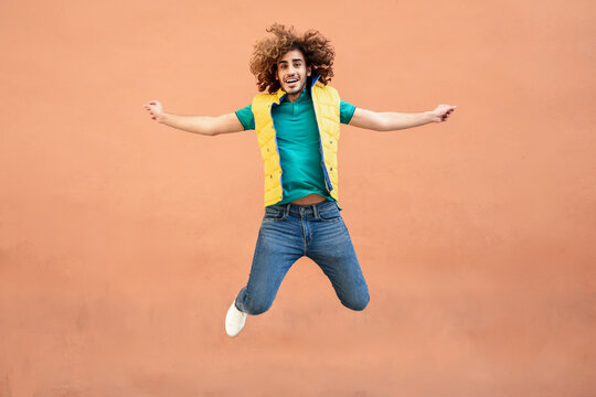 Portrait of smiling young man with curly hair wearing yellow waistcoat jumping in the air