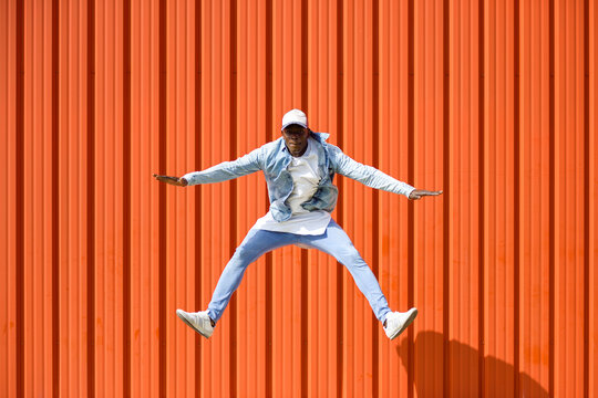 Man wearing casual denim clothes jumping in the air in front of orange wall