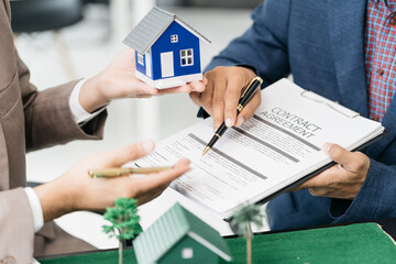 Real estate broker agent presenting and consult to customer to decision making sign insurance form agreement, home model, concerning mortgage loan offer in office.