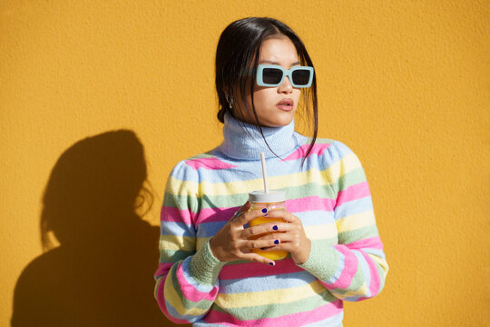 Young woman standing with orange juice in front of wall
