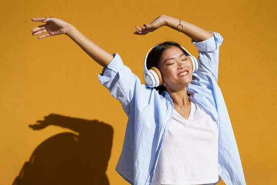Young woman with headphones listening to music enjoying in front of wall