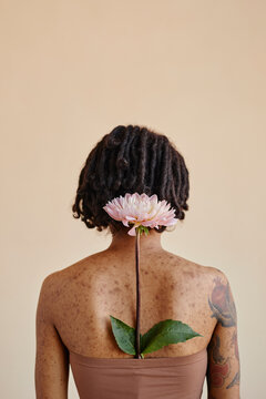 Young woman with flower in tube top against brown background
