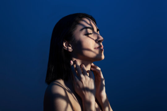 Smiling woman enjoying light on face against blue background