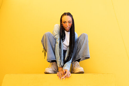 Woman with box braids crouching in front of yellow wall