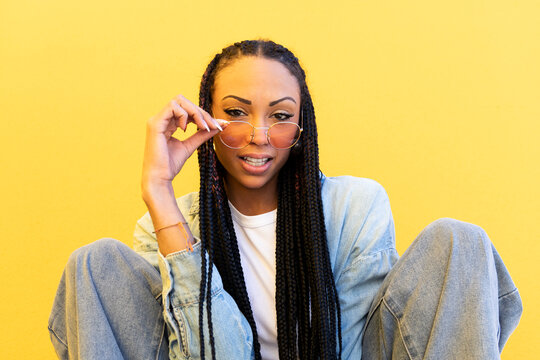Young woman wearing sunglasses in front of yellow wall