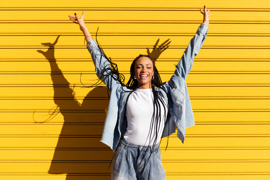 Cheerful woman standing with arms raised in front of yellow shutter