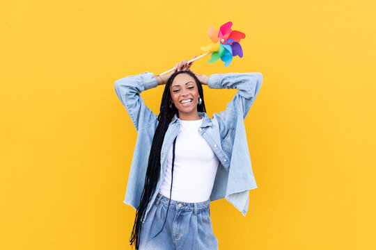 Cheerful woman holding pinwheel toy in front of yellow wall