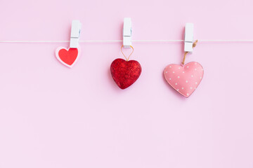 Red and pink heart hanging on a white wooden clothespin and white rope on pink background, Love and...
