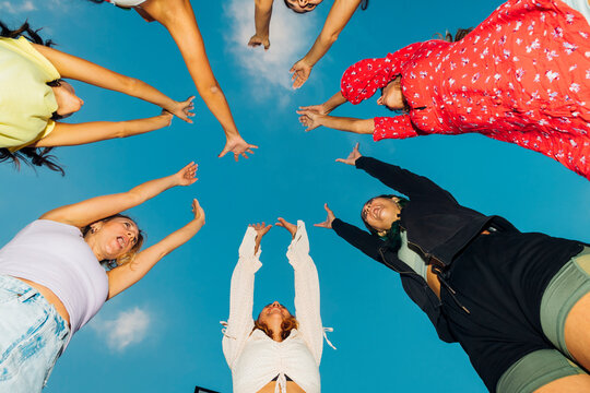 Female friends with arms raised under blue sky at dusk