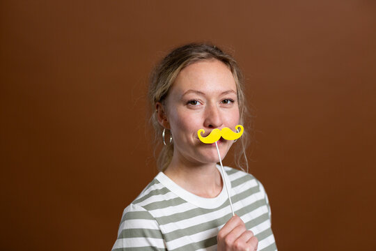 Blond woman holding mustache prop in studio