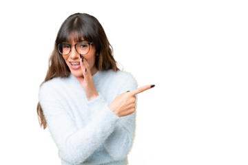 Young caucasian woman over isolated chroma key background pointing to the side to present a product and whispering something
