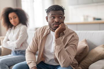 African spouses ignoring each other after quarrel sitting apart indoor - obrazy, fototapety, plakaty