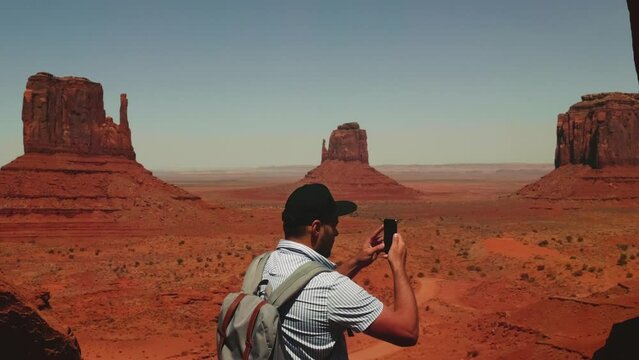Back view happy local man with backpack taking smartphone picture of incredible desert mountain view in Arizona USA.