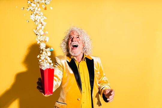 Cheerful senior man throwing popcorns against yellow background
