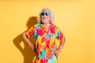 Happy senior man wearing sunglasses and standing with hands on hips against yellow background