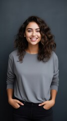 Obraz premium Portrait of young Mexican woman with pleasant smile and arms crossed isolated on gray wall with copy space Beautiful young woman with folded arms looking at camera against gray wall. isolated studio