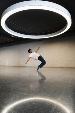 Young man with futuristic cyber glasses break dancing under modern ring lamp