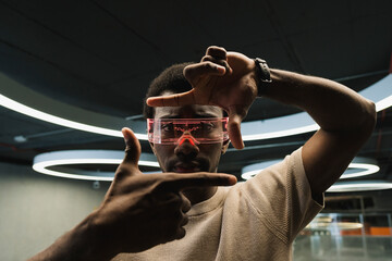 Young man with futuristic cyber glasses under modern ring lamp looking through finger frame