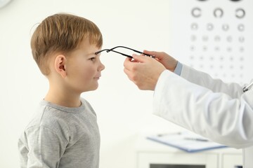 Vision testing. Ophthalmologist giving glasses to little boy indoors
