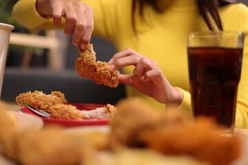 Happy young asian woman eating delicious fried chicken at home. Woman tearing fried chicken meat on...