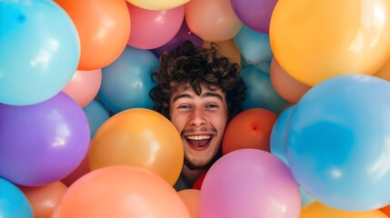 Fototapeta na wymiar Smiling young man looking at the camera, surrounded by a bunch of colorful balloons. Happy youthful male person, surprise party, celebration event, festival decoration