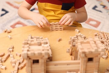Little boy playing with wooden construction set at table indoors, closeup. Child's toy - obrazy, fototapety, plakaty