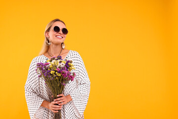 Portrait of smiling hippie woman with bouquet of flowers on yellow background. Space for text
