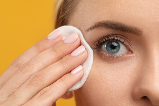 Beautiful woman removing makeup with cotton pad on orange background, closeup