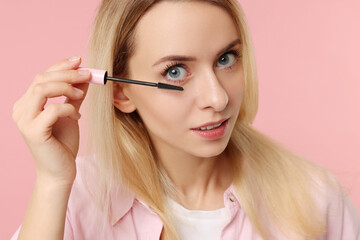 Fototapeta premium Beautiful woman applying mascara on pink background, closeup