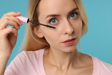 Beautiful woman applying mascara on light blue background, closeup