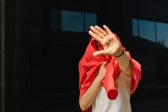 Businesswoman covered in red blazer gesturing stop sign on sunny day