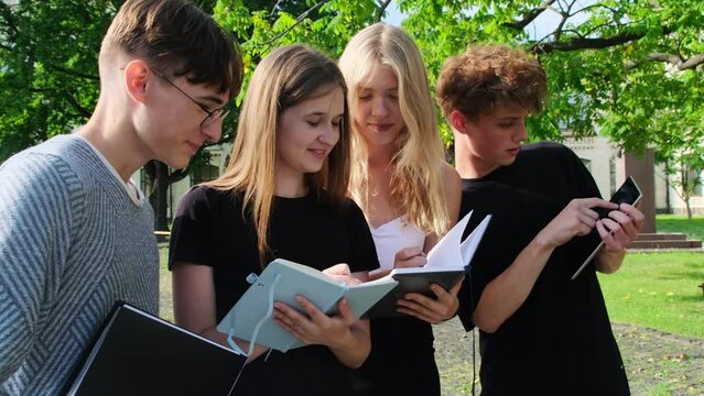 Concentrated student collaborates jotting down information in notebooks. Teenagers engage in collective dialogue on university campus