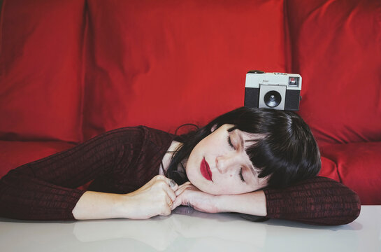 Woman resting on table with analog camera in front of red couch
